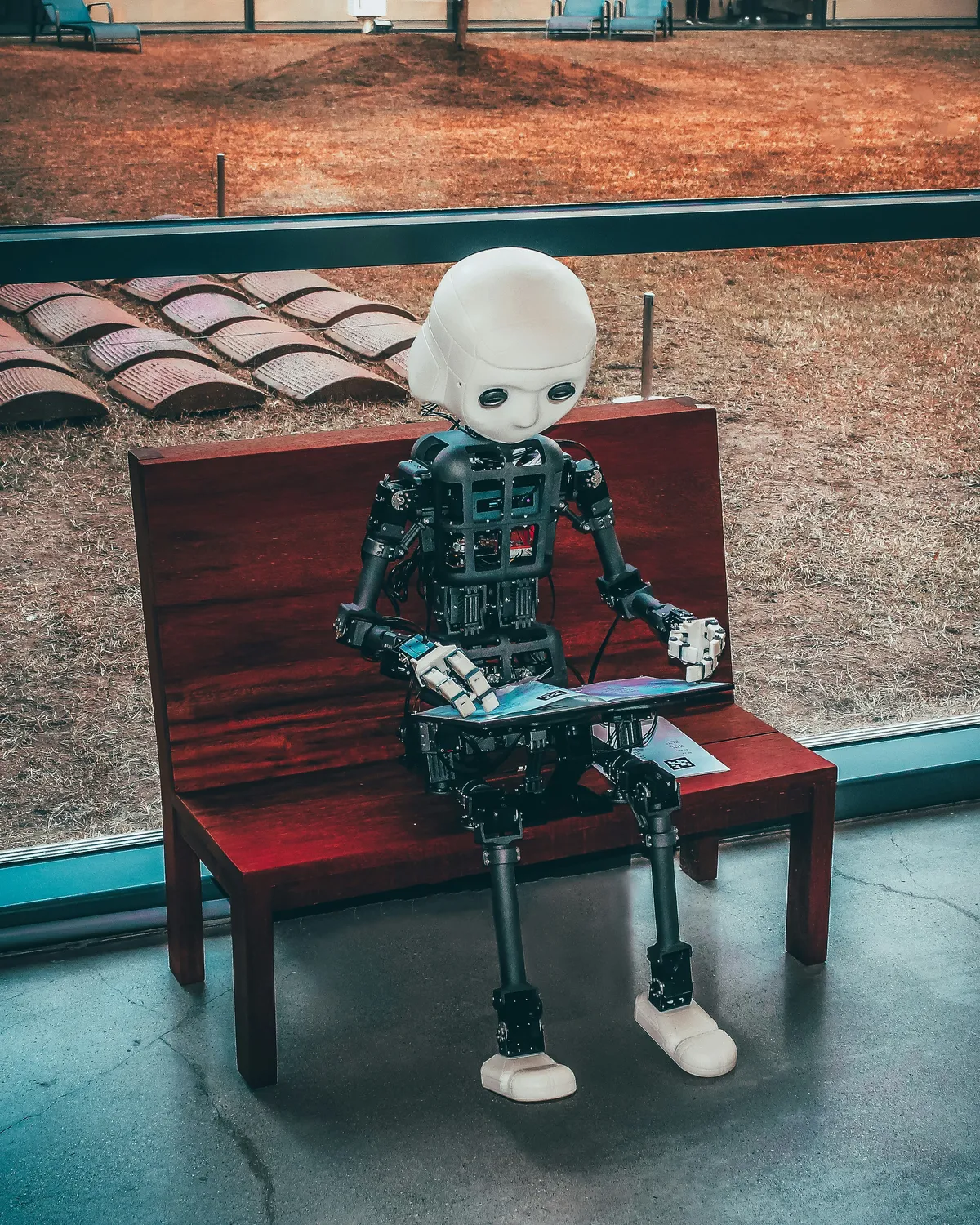 A humanoid robot sitting on a bench reading a tablet