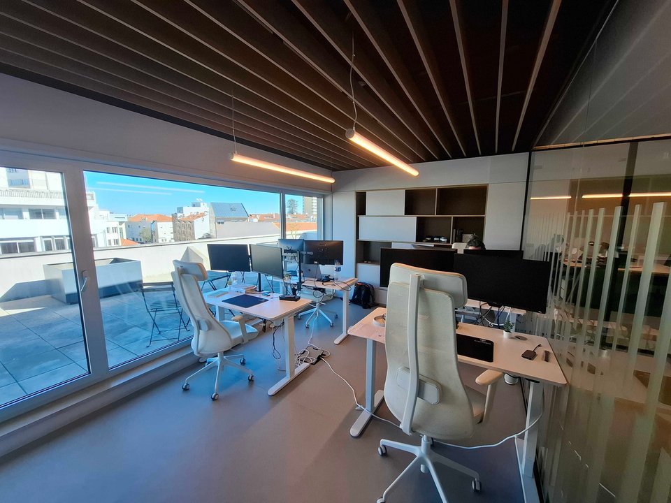 craftable software Aveiro office — standing desks with dual monitors and wooden slat ceiling overlooking the city