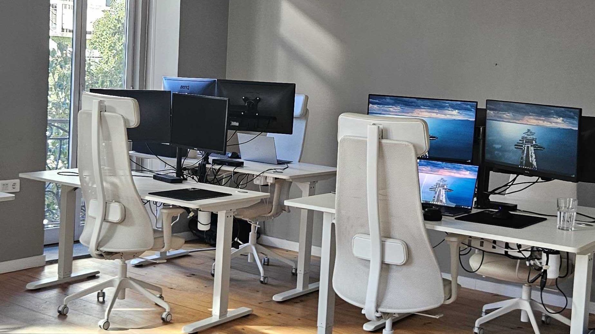 craftable software Porto office — standing desks with dual monitors and ergonomic chairs on warm wooden floors